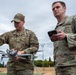 Two U.S. Air Force personnel in OCP (Operational Camouflage Pattern) uniforms are working with a commercial-style quadcopter drone on what appears to be an athletic field. The airman on the left, identified by name tape as 'Davidson,' is handling and preparing the drone, while the airman on the right holds a smartphone, likely for drone control or monitoring. The setting suggests a drone training or operational demonstration exercise.