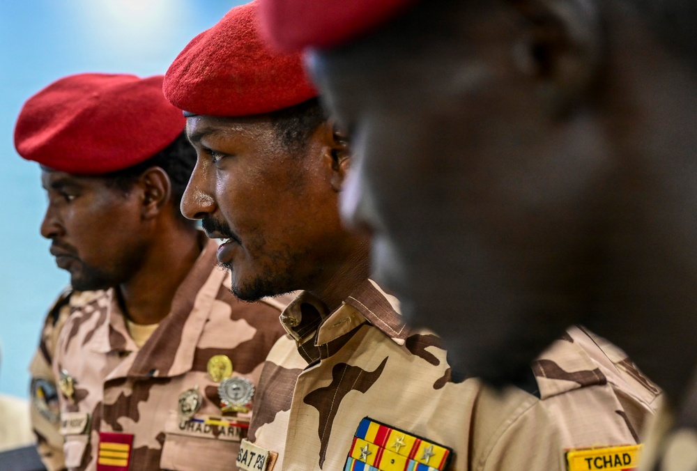 The image shows multiple military personnel wearing desert camouflage uniforms and distinctive red berets. At least one uniform displays a 'TCHAD' (Chad) patch and military ribbons/medals, indicating these are members of the Chadian armed forces. The individuals appear to be at a formal or official military event.
