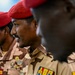 The image shows multiple military personnel wearing desert camouflage uniforms and distinctive red berets. At least one uniform displays a 'TCHAD' (Chad) patch and military ribbons/medals, indicating these are members of the Chadian armed forces. The individuals appear to be at a formal or official military event.
