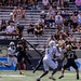 A college football game is in progress, showing an Army Black Knights quarterback wearing number 3 releasing a pass while under pressure from a defender wearing number 4 in white and green uniform. The ball is visible in mid-air above the players. Army players in black uniforms and opposing players in white/green uniforms are visible on the field, with a stadium crowd watching in the background.