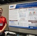 A young man named Alex Lawrence stands beside a large academic research poster at what appears to be a scientific conference or symposium. The poster presents 'SeptiBurnAlert,' an AI/ML tool integrated with qPCR assay to score the risk of burn sepsis from the first blood draw after ICU admission. The poster is affiliated with the Defense Health Agency (DHA) and WRAIR (Walter Reed Army Institute of Research).