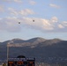 The image shows a football scoreboard for Herriman High School, displaying '2:59' on the game clock with a score of 0-0 between Herriman and Guest. Multiple military helicopters are visible flying in formation over a mountainous landscape. The scene appears to be a ceremonial flyover during a high school football game, with the scoreboard noting 'State Champions 2015'.