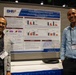 Two men are posing in front of a scientific research poster at what appears to be an academic or medical conference. The poster is titled 'Assessment of Mitochondrial Respiratory Parameters in Frozen TBI Samples: Extending its Utility in Military Medical Research' and is affiliated with the Defense Health Agency (DHA). Both individuals are wearing conference name badges, with visible names reading 'JIGNESH PANDYA' and 'HIREN MODI'.