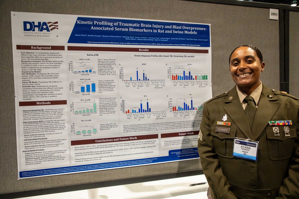 A U.S. Army soldier named Ayana Ferrer (visible on name tag) stands smiling beside a scientific research poster titled 'Kinetic Profiling of Traumatic Brain Injury and Blast Overpressure-Associated Serum Biomarkers in Rat and Swine Models.' The poster is affiliated with the Defense Health Agency (DHA) Research &amp; Development and Walter Reed Army Institute of Research. The setting appears to be an academic or military medical research conference.