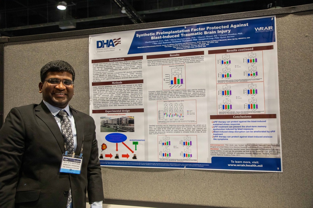 A man in a suit and tie stands beside a scientific research poster at what appears to be an academic or medical conference. The poster is titled 'Synthetic PreImplantation Factor Protected Against Blast-Induced Traumatic Brain Injury' and is affiliated with WRAIR (Walter Reed Army Institute of Research) and DHA (Defense Health Agency). The presenter is wearing a name badge and smiling for the photo.