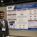 A man in a suit and tie stands beside a scientific research poster at what appears to be an academic or medical conference. The poster is titled 'Synthetic PreImplantation Factor Protected Against Blast-Induced Traumatic Brain Injury' and is affiliated with WRAIR (Walter Reed Army Institute of Research) and DHA (Defense Health Agency). The presenter is wearing a name badge and smiling for the photo.