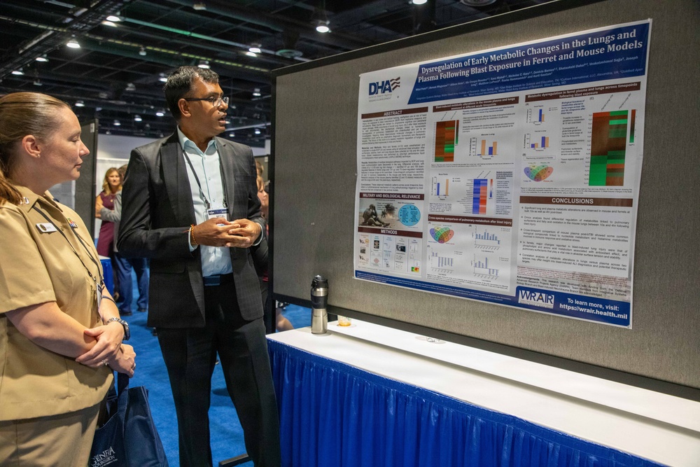 Two individuals are viewing a scientific research poster at what appears to be a military or defense health conference. The poster, displayed under DHA (Defense Health Agency) and WRAIR (Walter Reed Army Institute of Research) branding, presents research titled 'Dysregulation of Early Metabolic Changes in the Lungs and Plasma Following Blast Exposure in Ferret and Mouse Models.' A man in a dark suit appears to be presenting or discussing the poster with a woman in a military tan uniform.