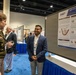 A military officer in Army dress uniform with Airborne patch is engaged in conversation with a civilian researcher at an academic poster session. The research poster, affiliated with DHA (Defense Health Agency) and WRAIR (Walter Reed Army Institute of Research), presents findings on 'Serum levels of lung-specific proteins as pulmonary injury after blast exposure.' The setting appears to be a formal military medical or scientific conference.