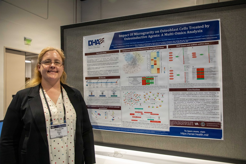A woman named Allison Hoke stands beside a scientific research poster at what appears to be an academic or military health conference. The poster is titled 'Impact of Microgravity on Osteoblast Cells Treated by Osteoinductive Agents: A Multi-Omics Analysis' and is affiliated with the Defense Health Agency (DHA). She is wearing a name badge and posing next to her research presentation.