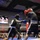 Two boxers are actively competing in a boxing ring during what appears to be a military-themed boxing event called 'Phantom Warriors.' The fighter on the left wearing black shorts and blue gloves is throwing a punch at the opponent on the right who is wearing red gloves and a dark blue outfit. A crowd of spectators is visible in the background along with a display screen showing fighter profiles.
