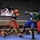 Two boxers are competing in a boxing ring during what appears to be a military boxing event called 'Phantom Warriors vs Phantom Lethal.' One boxer wearing red gear and 'Title Boxing' shorts is exchanging punches with an opponent in blue gear and a green shirt. A crowd of spectators watches from ringside, and a scoreboard/display screen in the background shows fighter profiles labeled 'Webb' and 'Jackson' in the Middleweight category.
