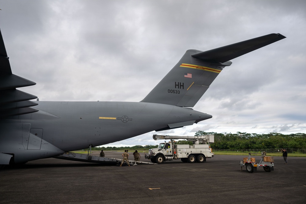 A U.S. Air Force C-17 Globemaster III military cargo aircraft with tail code 'HH' and serial number 00533 is parked on a tarmac in what appears to be a tropical location. Ground crew personnel are actively working around the aircraft's rear cargo ramp area, with support vehicles including a utility truck present. The 'HH' tail code indicates the aircraft is assigned to Hickam Field (Joint Base Pearl Harbor-Hickam), Hawaii.
