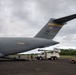 A U.S. Air Force C-17 Globemaster III military cargo aircraft with tail code 'HH' and serial number 00533 is parked on a tarmac in what appears to be a tropical location. Ground crew personnel are actively working around the aircraft's rear cargo ramp area, with support vehicles including a utility truck present. The 'HH' tail code indicates the aircraft is assigned to Hickam Field (Joint Base Pearl Harbor-Hickam), Hawaii.