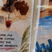 The image shows two printed artworks or posters placed side by side, partially wrapped in plastic. The left poster features a watercolor-style illustration of a person holding an iced coffee drink, accompanied by the text 'Come for the coffee, stay for the moments.' The right poster appears to depict a cityscape with blue skies and tall buildings.