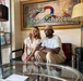 Two people are seated together on a black leather sofa inside a lounge cafe called 'Lounge Full Cafe Château,' posing for a photo. The interior features eclectic decor including stained glass panels, floor lamps, and a glass coffee table in the foreground. The atmosphere appears casual and relaxed.