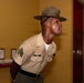 A U.S. Marine Corps Drill Instructor in service uniform is photographed in a leaning forward posture, appearing to be issuing commands or instructions. The Marine wears the distinctive Drill Instructor campaign cover (cover/hat) and displays the rank of Staff Sergeant on the left sleeve. The name tape reads 'REDD' and several service ribbons are visible on the chest.