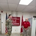 Two individuals stand in an official U.S. Army Corps of Engineers Emergency Operations room. One person is wearing U.S. Army combat uniform (OCP/multicam) and the other is wearing a red polo shirt with what appears to be a U.S. Army Corps of Engineers logo. They appear to be engaged in a formal or semi-formal interaction, possibly a briefing or recognition ceremony.
