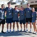 Six individuals wearing matching gray t-shirts with unit patches are posing together in front of a building labeled 'Civil Engineers.' All six are wearing gold medals on red, white, and blue ribbons, suggesting they recently competed in and won a sporting or fitness event. The group appears to be affiliated with a military or civil engineering unit.