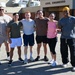 Six individuals in athletic/casual workout attire pose together in front of a building labeled 'Civil Engineers,' likely a military or government facility. The group appears to be in good spirits after a physical training or fitness activity, smiling and standing arm-in-arm. The setting suggests this may be a military base civil engineering unit.