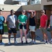 A group of six people pose together outdoors in front of a building partially labeled 'Civil Engi...' (likely Civil Engineering). They are dressed in athletic/casual wear, suggesting a fitness or recreational activity. One person on the left is giving a shaka/thumbs-up gesture, and the group appears to be in good spirits.