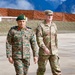 Two military officers — one from the Indian Army and one from the U.S. Army — are walking together on what appears to be a tarmac or parade ground with mountainous terrain visible in the background. The Indian officer wears a green beret and name tape reading 'AMARESH GUNJAN' with lieutenant general rank insignia, while the U.S. officer's name tape reads 'JACKMAN' with 'US ARMY' and a colonel's eagle rank insignia. The setting and uniforms suggest a bilateral military engagement or joint exercise.