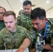 Military personnel from multiple nations are gathered around a table reviewing documents or a laptop in what appears to be an indoor briefing or planning session. An Australian soldier identified as 'Roberts' is seated at the center, surrounded by Indonesian Army (TNI AD) soldiers including individuals named 'Suhardi' and 'Canyo'. The setting and lanyards suggest this is part of a multinational military exercise, specifically 'Latgabma Super Garuda Shield Tahun 2026'.