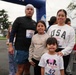 A family of four poses together at a 'Remembrance Run' event, standing near the starting/finishing arch. The group consists of two adults and two children, all wearing race bibs. The event appears to be a community running event held outdoors on an overcast day.