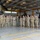Polish General Piotr Trytek Strengthens Alliance During 12th CAB Visit A group of approximately 18-20 military personnel in camouflage uniforms pose for a formal group photograph inside a military aviation hangar. Two military helicopters are visible in the background — a large CH-47 Chinook tandem-rotor helicopter on the left and what appears to be a UH-60 Black Hawk or AH-64 Apache on the right. The setting appears to be an official visit or unit photo opportunity.