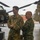 Polish General Piotr Trytek Strengthens Alliance During 12th CAB Visit Two military personnel in different camouflage uniforms stand together on a helicopter flight line or tarmac. The taller individual wears a U.S. Army uniform with the name tape 'SCHOONOVER,' while the second individual wears a woodland camouflage pattern with what appears to be a Polish flag patch. They appear to be engaged in a briefing or discussion near military equipment, with CH-47 Chinook helicopters visible in the background.