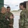 Polish General Piotr Trytek Strengthens Alliance During 12th CAB Visit Three military personnel are engaged in a discussion near a briefing board labeled 'Intelligence/AMSO Integration' at what appears to be a military aviation facility. One individual wears a Polish military uniform with a Polish flag patch, while the other two wear U.S. Army OCP (Operational Camouflage Pattern) uniforms, one identified by a name tape reading 'BOLTEN'. A helicopter is visible in the background on the airfield.