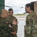Three military personnel are engaged in a discussion near a briefing board labeled 'Intelligence/AMSO Integration' at what appears to be a military aviation facility. One individual wears a Polish military uniform with a Polish flag patch, while the other two wear U.S. Army OCP (Operational Camouflage Pattern) uniforms, one identified by a name tape reading 'BOLTEN'. A helicopter is visible in the background on the airfield.