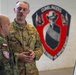 Two military personnel are engaged in a briefing or discussion near a whiteboard with written notes. One soldier wears a US Army uniform with the name tape 'BILLMIRE' and Sergeant rank insignia, while the other wears a Polish military camouflage uniform with a Polish flag patch. They are standing in front of a unit insignia mural reading 'GUNSLINGERS' with the motto 'NO FRIEND NO WORSE ENEMY'.