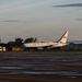 A United States of America government aircraft, consistent with an Air Force executive transport, is parked on a tarmac at what appears to be a military airfield. The aircraft features the distinctive blue and white livery with 'UNITED STATES OF AMERICA' lettering and an American flag on the tail. The image is taken during golden hour (early morning or late evening), with hangars and trees visible in the background.