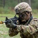 A U.S. Army soldier in full combat gear is aiming a rifle in an outdoor training environment. The soldier is wearing MultiCam (OCP) camouflage uniform, a tactical helmet with accessories, and has face paint applied. Visible unit patches and helmet markings suggest an active-duty or National Guard assignment.