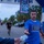 Katterbach Community and German Partners Commemorate 9/11 with Memorial Run and Ceremony A runner wearing a blue USO t-shirt is crossing or approaching a finish line at what appears to be a charity or military-affiliated 5K/fun run event. He is reaching out to accept a water bottle being handed to him by a volunteer. The event is co-sponsored by USO and MWR (Morale, Welfare, and Recreation), suggesting a military installation setting.