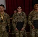 Three U.S. Army soldiers in OCP (Operational Camouflage Pattern) uniforms pose together at what appears to be an awards ceremony. The soldier on the left (Silva) wears a medal with a gold ribbon, while the soldiers in the center (Jansma) and right (Jimenez) hold dark plaques. The setting appears to be an indoor venue with red curtains in the background.