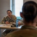 Two U.S. Army soldiers in OCP (Operational Camouflage Pattern) uniforms are seated across from each other at a table in what appears to be a military facility or office setting. The soldier facing the camera, identified by name tape as 'HALE,' appears to be engaged in a briefing, counseling session, or interview. Documents, a water bottle, and a tumbler are visible on the table between them.