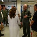 A group of military personnel and civilians are gathered inside what appears to be a laboratory or research facility. A senior officer in an olive green flight suit is speaking to a person in a white lab coat and a civilian, while other uniformed personnel observe in the background. The setting suggests an official tour or briefing of a scientific or medical facility.