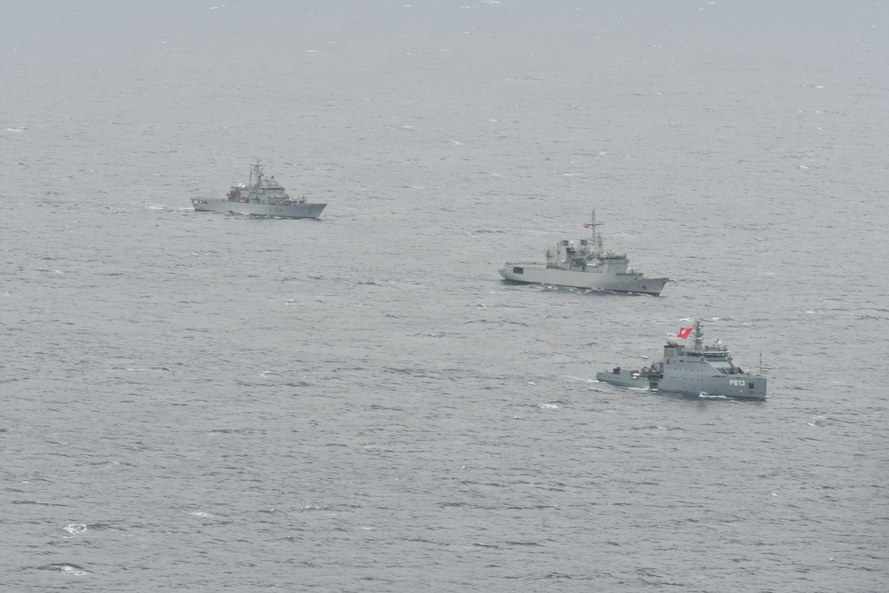 Three naval vessels are sailing in formation across open ocean under overcast, hazy conditions. The ships appear to be gray-painted military vessels of varying sizes, with the closest vessel bearing the hull number 'P813' and a red flag. The formation suggests a coordinated naval exercise or patrol operation.