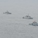 Three naval vessels are sailing in formation across open ocean under overcast, hazy conditions. The ships appear to be gray-painted military vessels of varying sizes, with the closest vessel bearing the hull number 'P813' and a red flag. The formation suggests a coordinated naval exercise or patrol operation.