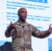 A U.S. Army officer with the name tag 'CLARK' and four-star general rank insignia is delivering a presentation in front of a projected slide about 'Partnerships.' He is gesturing with both hands raised, appearing engaged in active speech. The slide behind him emphasizes that partnerships are a strategic advantage that adversaries cannot replicate.