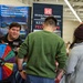 A recruiter or representative from the US Army Corps of Engineers (Walla Walla district) is engaging with two visitors at what appears to be a career fair or recruitment event. The representative is using a colorful prize/trivia spin wheel as an interactive engagement tool. Banners in the background reference engineering projects across Idaho and the Pacific Northwest.