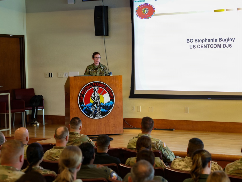 Brigadier General Stephanie Bagley, US CENTCOM DJ5, is delivering a presentation at the 163rd Regional Training Institute. She stands at a wooden podium addressing an audience of military personnel in uniform. The slide behind her identifies her name and title, and the presentation is marked 'UNCLASSIFIED'.