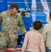 A U.S. Army officer identified as 'Droesch' from the Walla Walla District is speaking with two civilian visitors at a recruitment or informational booth. The display features U.S. Army Corps of Engineers materials highlighting missions including hydropower, navigation, flood risk management, and environmental stewardship. The booth includes a 'Build Beyond Yourself' recruitment banner with a QR code.