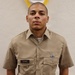 A young male service member in a khaki military uniform stands at attention in front of a white textured wall. He wears a name tag reading 'LEGGIN' on his left chest pocket and a small ribbon device on his right chest pocket. A tattoo is visible on his right forearm.