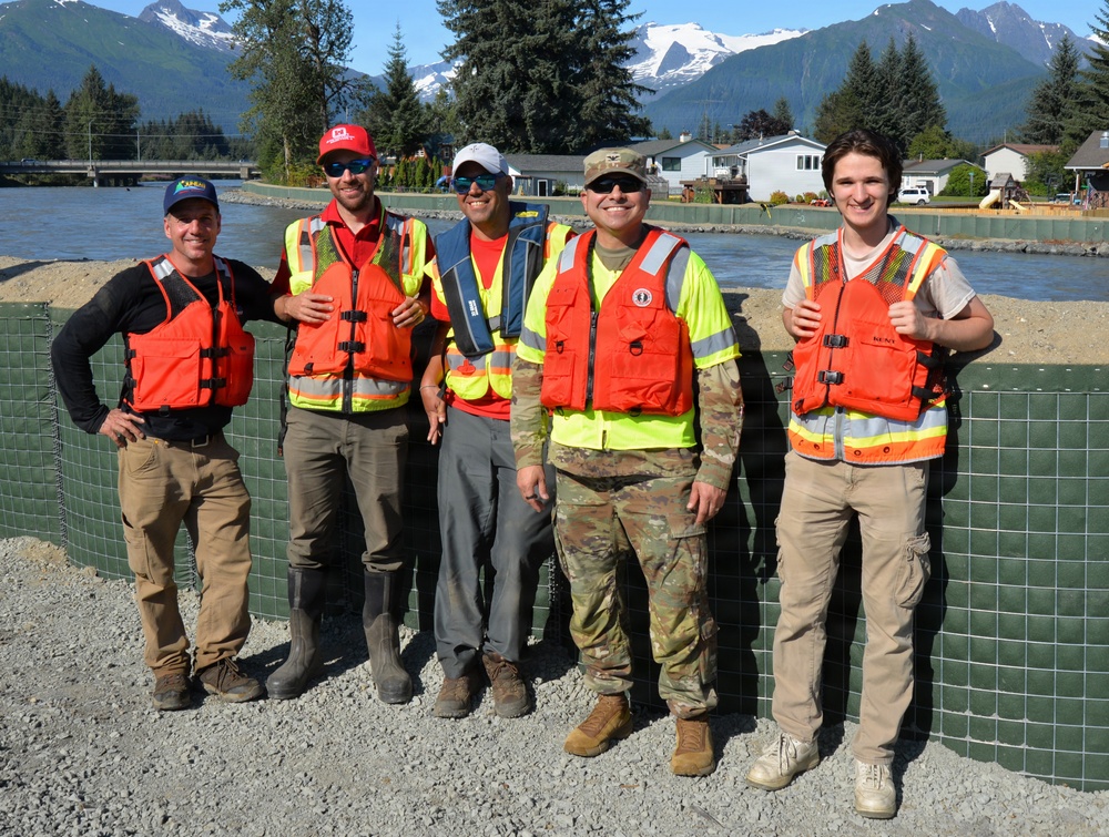 Members of the USACE and City and Borough of Juneau team pose for a photo in front of the flood barrier project while performing spot checks during the glacial lake outburst flood