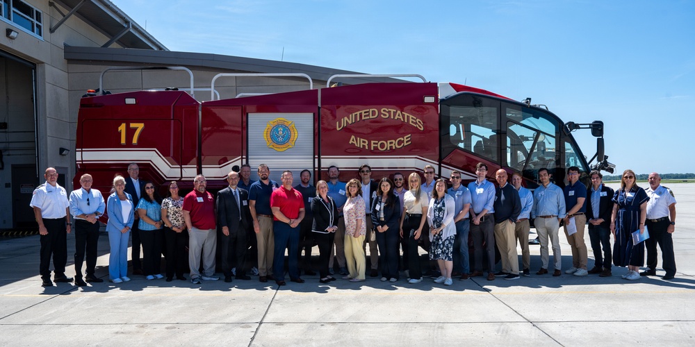 A large group of approximately 30 civilians and personnel pose for a group photograph in front of a United States Air Force fire truck numbered '17'. The event appears to be an official visit, tour, or community engagement event at a U.S. Air Force installation. The participants are dressed in business casual and professional attire, suggesting a civilian outreach or leadership program.