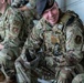 The image shows multiple U.S. Air Force Security Forces personnel in OCP (Operational Camouflage Pattern) uniforms seated together, likely during a briefing or rest period. The central figure, identified by a name tape reading 'BROWN,' is wearing a beret with a unit insignia, a tactical vest, and tactical gloves, and appears to be smiling. The personnel display Security Forces ('SF') patches and unit insignia patches on their uniforms.