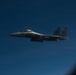 A U.S. Air Force F-15 Eagle fighter jet is photographed in flight against a deep blue sky. The aircraft bears the tail code 'SJ' and serial number '499', identifying it as belonging to Seymour Johnson Air Force Base in North Carolina. The image appears to have been taken from another aircraft, likely during a formation flight or aerial refueling operation.