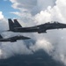 Two U.S. Air Force F-15E Strike Eagle fighter jets are flying in formation above a cloud layer. Both aircraft bear the 'SJ' tail code, indicating they belong to the 4th Fighter Wing based at Seymour Johnson Air Force Base, North Carolina. The foreground aircraft displays the serial number 11674 and appears to be carrying external ordnance or fuel tanks on its hardpoints.